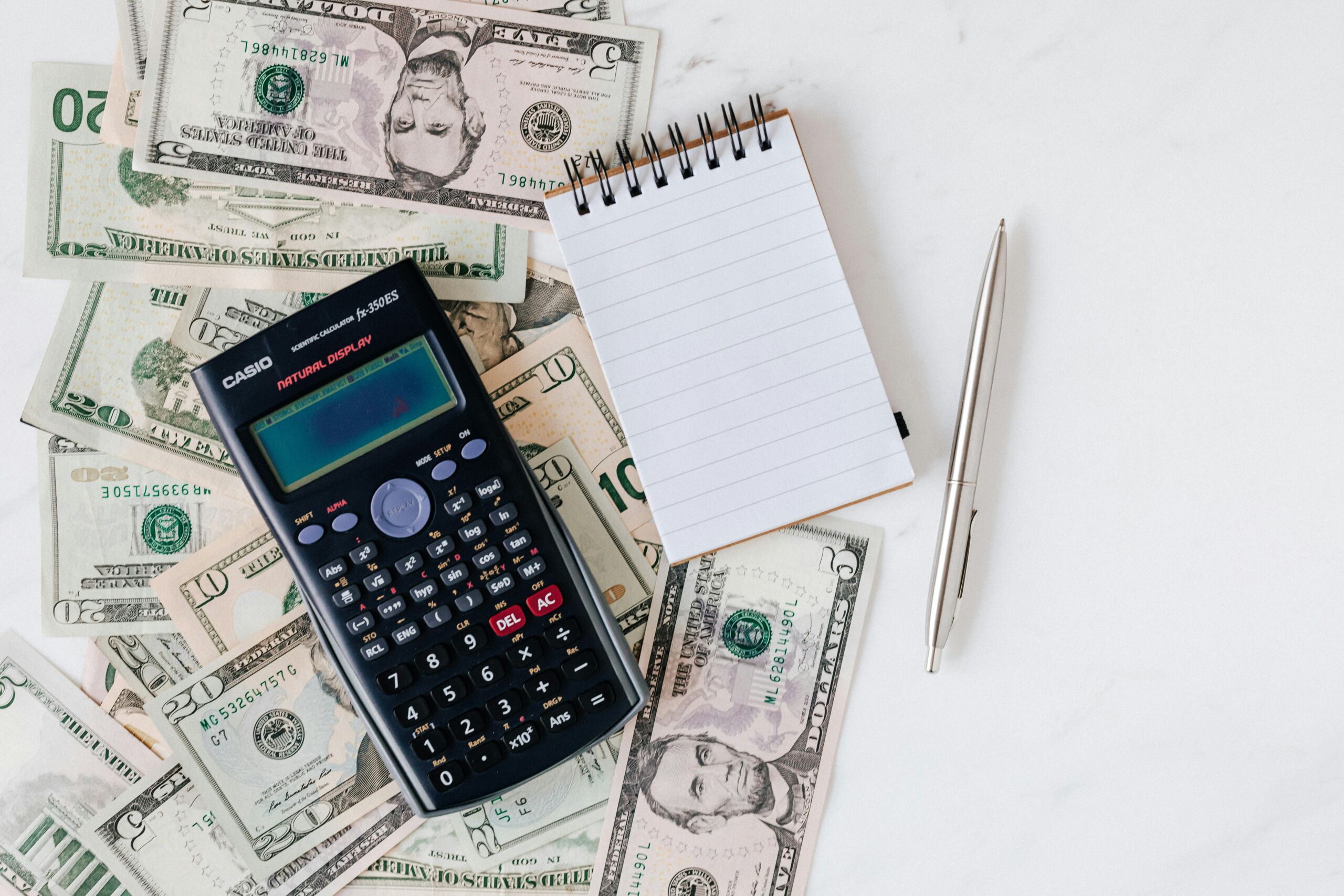 A calculator, notepad, and a bunch of cash on a table.