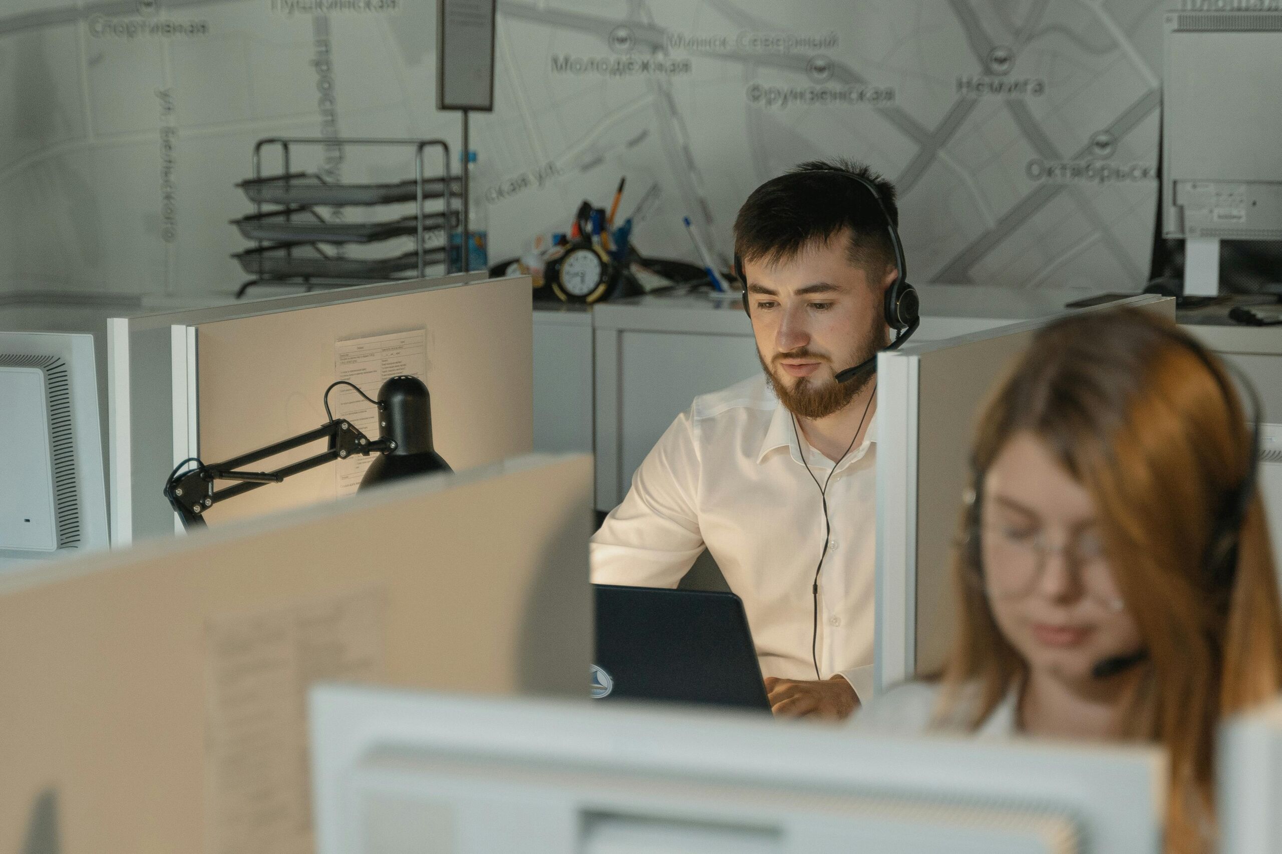 A man is working at his office cubicle wearing headphones and has a focused face.